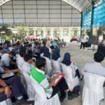 Pelajar SMK duduk berderet mendengarkan pemateri di aula terbuka, dengan spanduk DPMPTSP OTW di sisi kanan