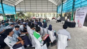Pelajar SMK duduk berderet mendengarkan pemateri di aula terbuka, dengan spanduk DPMPTSP OTW di sisi kanan
