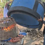 Tiga pria menutup api yang membakar kurungan bambu dengan drum biru di pekarangan berumpun bambu